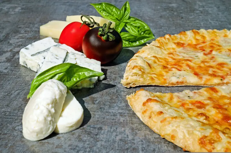Close-up of pizza with cheese slices, tomatoes, basil on a stone surface