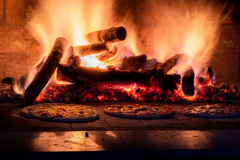 Rustic wood-fired pizza oven with flames and pizzas baking, capturing the warmth of traditional cooking