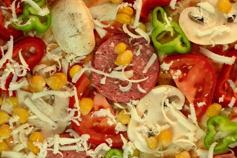 A detailed top view of colorful unbaked pizza ingredients featuring vegetables and toppings