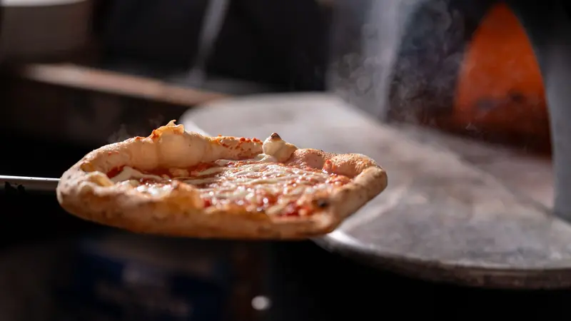 Close-up of a steaming hot pizza fresh from a wood-fired oven, showcasing melted cheese and crispy crust