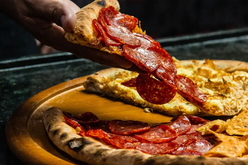 Fresh pepperoni pizza slice being lifted from a wooden board by hand. Tasty and mouth-watering dinner option