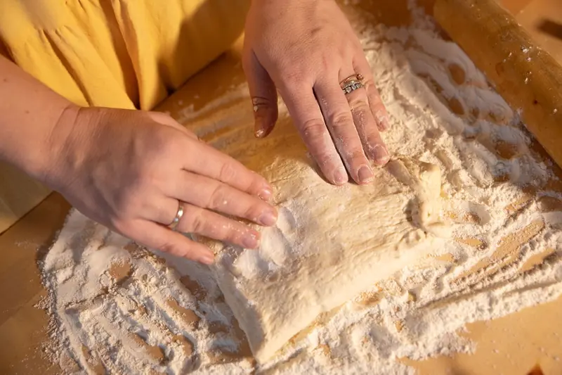 Close-up of hands kneading dough on a wooden surface with flour