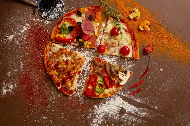 Flat lay of four assorted pizza slices with varied toppings on a flour-dusted surface