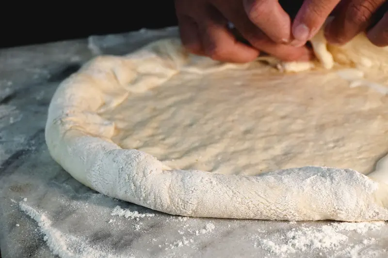 A close-up view of hands preparing pizza dough on a marble surface, showcasing the art of homemade pizza making