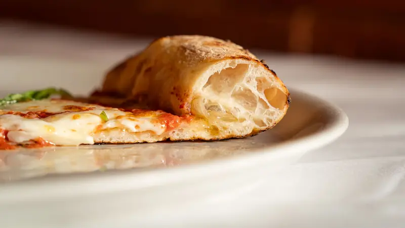 A detailed view of a fresh margarita pizza slice on a white plate, showing melted cheese and crust texture