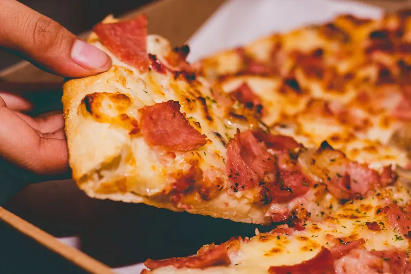 Close-up of a hand holding a delicious slice of pepperoni pizza