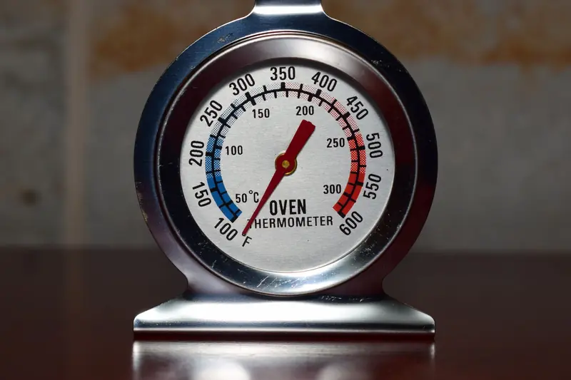 Close-up of a metallic oven thermometer showing temperature in Celsius and Fahrenheit