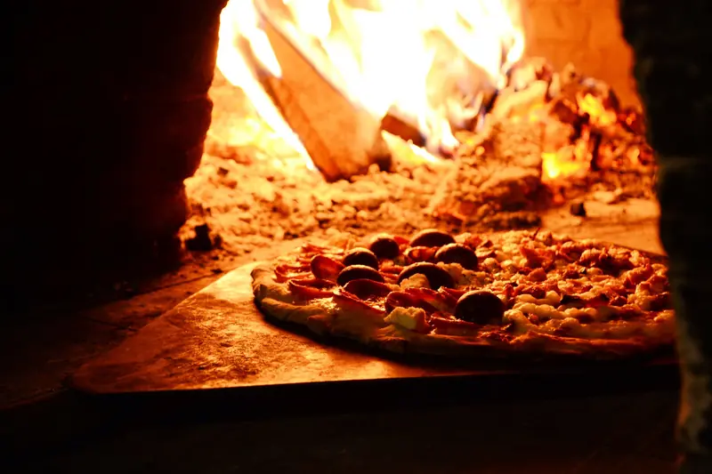 Delicious pizza baking in a traditional wood-fired oven with vibrant flames