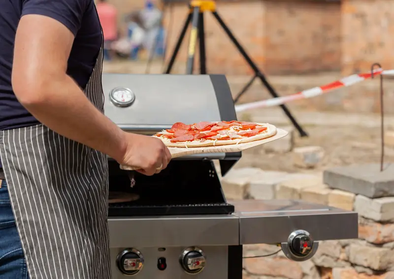 Man grilling a homemade pizza with pepperoni on an outdoor barbecue grill