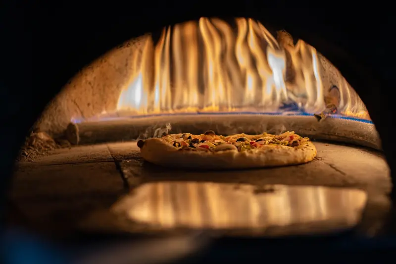 A delicious pizza baking in a traditional wood-fired oven with vibrant flames
