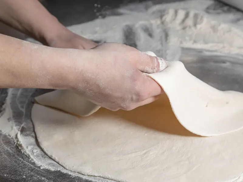 Close-up of hands preparing pizza dough on a floured surface, showcasing culinary skills